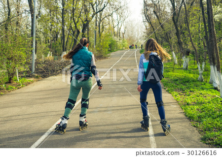 Two girls on roller skates ride along the road Two girls on roller skates ride along the road 30126616