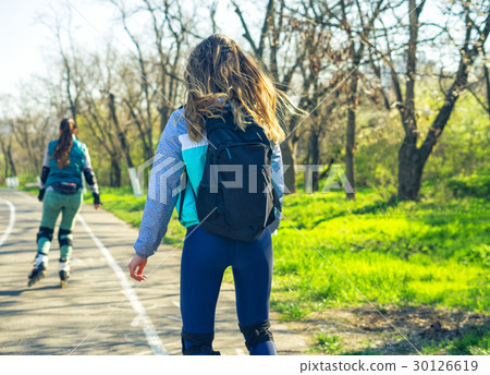 Two girls on roller skates ride along the road Two girls on roller skates ride along the road 30126619