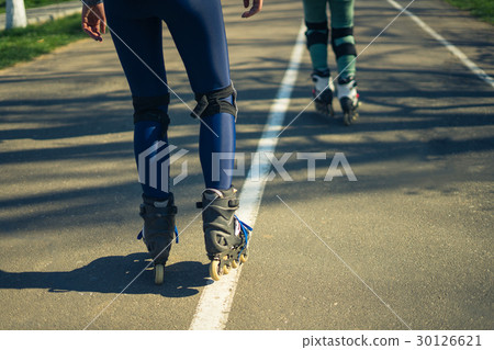 Two girls on roller skates ride along the road Two girls on roller skates ride along the road 30126621