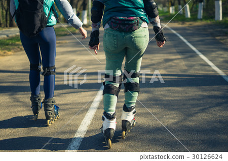 Two girls on roller skates ride along the road Two girls on roller skates ride along the road 30126624