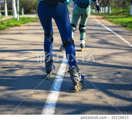 Two girls on roller skates ride along the road Two girls on roller skates ride along the road 30126625