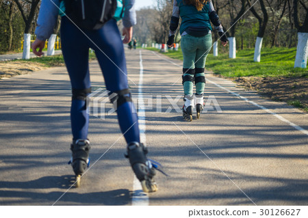 Two girls on roller skates ride along the road Two girls on roller skates ride along the road 30126627