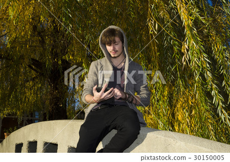 Teenager reading electronic book in a sunny day Teenager reading electronic book in a sunny day 30150005
