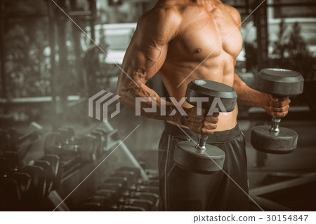muscular young man lifting weights in gym  30154847