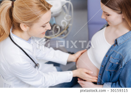 Kind obstetrician examining pregnant belly in the Kind obstetrician examining pregnant belly in the 30159315