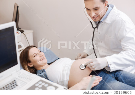 Amused pregnant woman enjoying belly checkup in Amused pregnant woman enjoying belly checkup in 30159605
