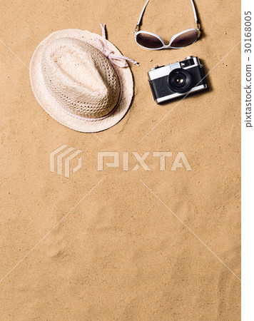 Sunglasses, wicker hat and camera. Sand background 30168005