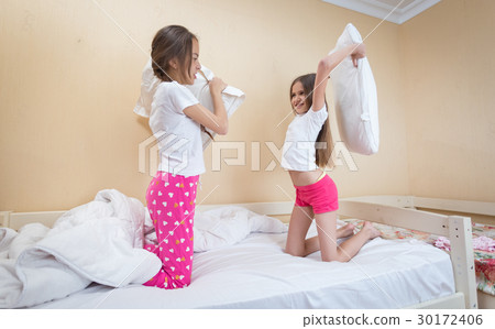 Two girls in pajamas having fun at pillow fighting Two girls in pajamas having fun at pillow fighting 30172406