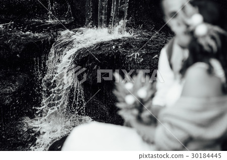 couple hugging sitting on the stone at waterfall couple hugging sitting on the stone at waterfall 30184445