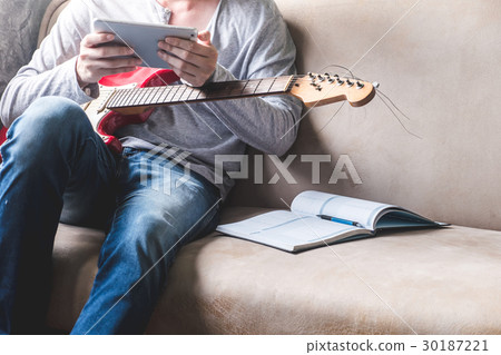 man using tablet with guitar and notebook on sofa man using tablet with guitar and notebook on sofa 30187221
