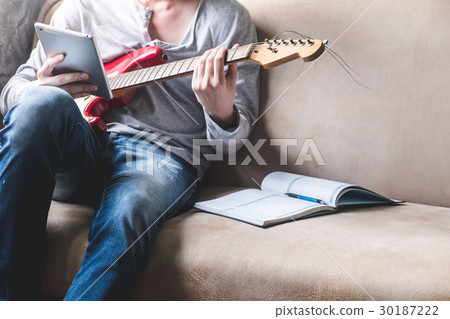 man using tablet with guitar and notebook on sofa man using tablet with guitar and notebook on sofa 30187222