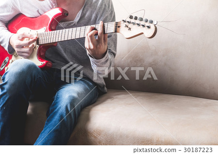 Casual young man playing guitar on sofa at home. 30187223
