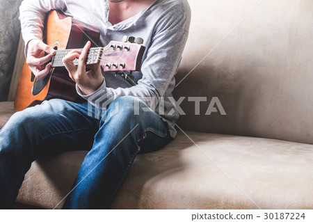 Casual young man playing guitar on sofa at home. Casual young man playing guitar on sofa at home. 30187224