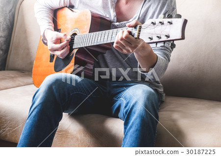 Casual young man playing guitar on sofa at home. Casual young man playing guitar on sofa at home. 30187225