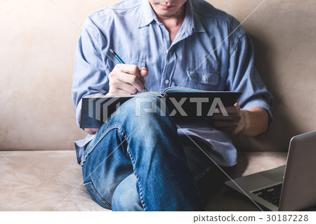 man writing some data in notebook on sofa 30187228