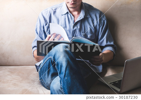 Casual young man reading documents on sofa Casual young man reading documents on sofa 30187230