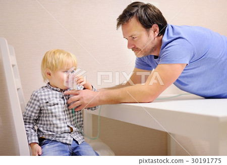 Middle age father helping his toddler son with inhalation therapy by the mask of inhaler Middle age father helping his toddler son with inhalation therapy by the mask of inhaler 30191775