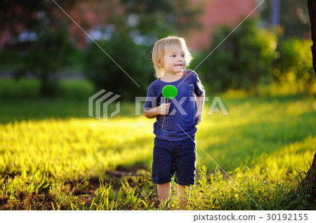 Cute toddler boy with big green lollipop at sunny park Cute toddler boy with big green lollipop at sunny park 30192155