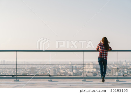 Woman using mobile phone at rooftop during sunset Woman using mobile phone at rooftop during sunset 30195195