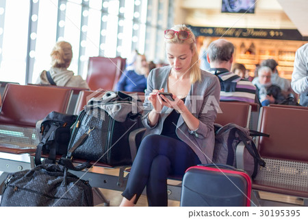 Female traveler using cell phone while waiting on 30195395