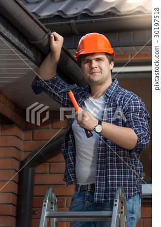 Worker in hardhat with hammer on step ladder 30197518