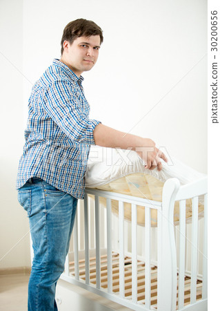 Father putting mattress in baby's cot at nursery 30200656