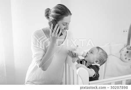 Woman talking by phone and feeding baby Woman talking by phone and feeding baby 30207898
