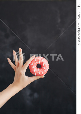 Pink donut in a woman's hand on black background Pink donut in a woman's hand on black background 30220810