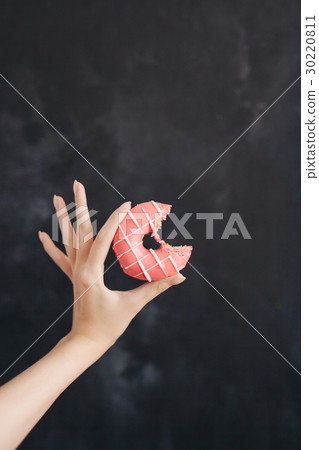 Pink donut in a woman's hand on black background 30220811