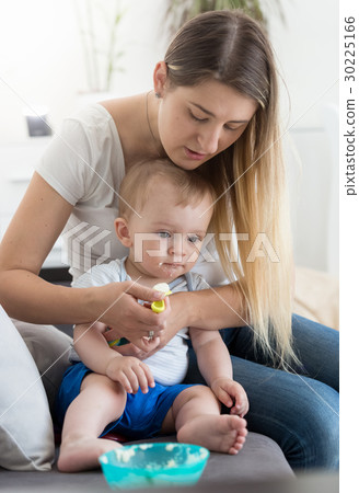 Mother sitting on sofa and feeding her baby Mother sitting on sofa and feeding her baby 30225166