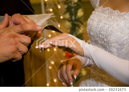 Groom putting a wedding ring on bride's finger 30231673