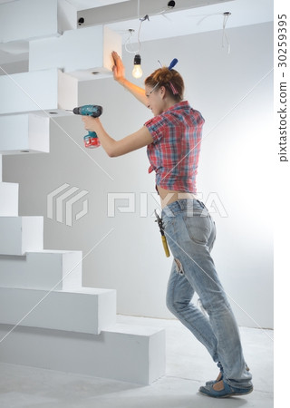 Beautiful young woman uses an electric drill Beautiful young woman uses an electric drill 30259395