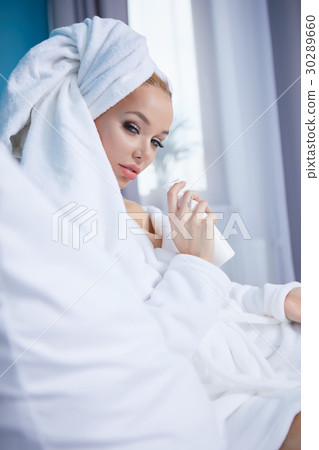 A woman in a bathrobe and a towel on her head lies on a bed 30289660
