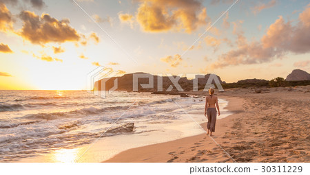 Woman walking on sandy beach at sunset. 30311229
