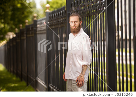 Fashion bearded hipster posing next to a fence 30315246