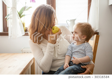 Mother and son at the kitchen eating an apple 30316584