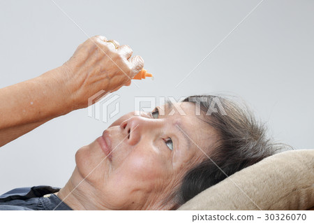 elderly woman applying eye drops on bed 30326070