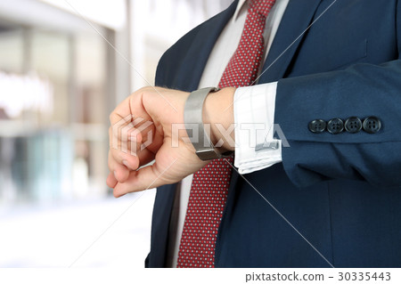 Businessman checking time on his watch at office Businessman checking time on his watch at office 30335443