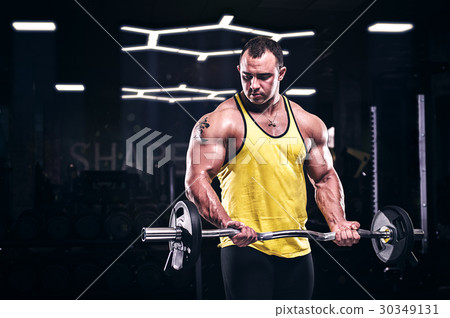 Muscular bodybuilder doing biceps exercise in gym 30349131