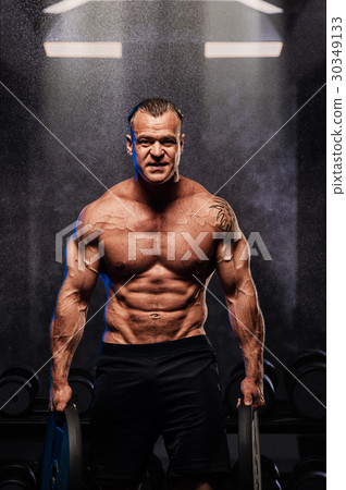 Muscular bodybuilder posing with weights in gym. 30349133