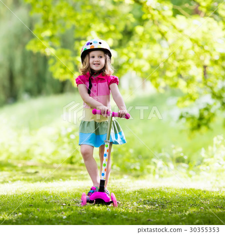 Little girl riding a colorful scooter Little girl riding a colorful scooter 30355353