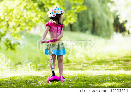 Little girl riding a colorful scooter Little girl riding a colorful scooter 30355354