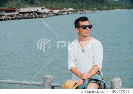 Guy sits on the railing of the pier in a white 30357031