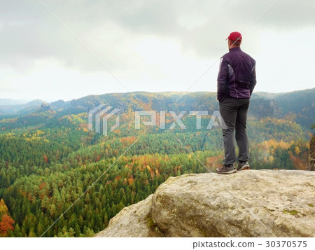 Hiker on rock end above valley, watch over mist Hiker on rock end above valley, watch over mist 30370575