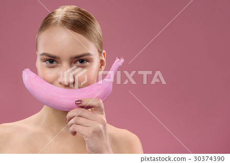 Smiling cute girl making fun with pink banana Smiling cute girl making fun with pink banana 30374390
