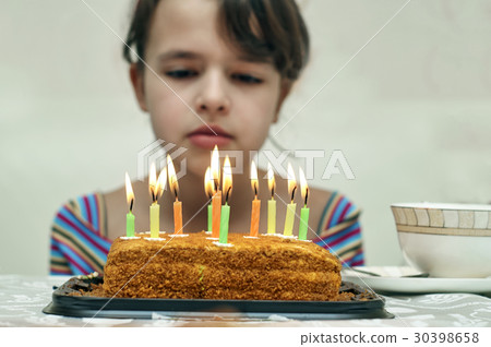 Girl looking at birthday cake with burning candles Girl looking at birthday cake with burning candles 30398658