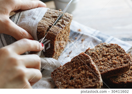The girl cuts whole-wheat rye bread on a wooden The girl cuts whole-wheat rye bread on a wooden 30411602