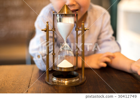 Asian child looking at hourglass on the table 30412749