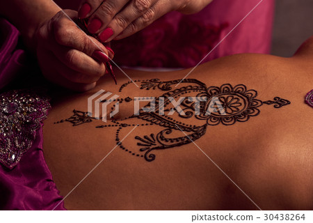 Mehendi artist paints an ornament of henna on an eastern girl 30438264