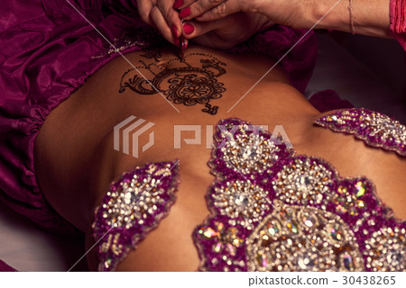 Mehendi artist paints an ornament of henna on an eastern girl Mehendi artist paints an ornament of henna on an eastern girl 30438265